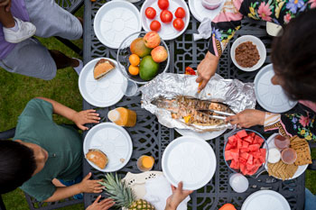 ariel view of family gathered around outdoor meal with grilled fish, watermelon and fresh tomatos