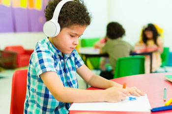 Child wearing headphones draws alone in a classroom.