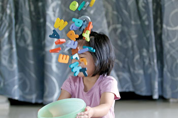 A young child tosses a bowl full of foam alphabet letters into the air.