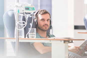Young adult male sitting in chair wearing headphones while receiving chemotherapy.
