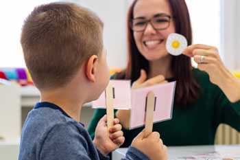speech-language pathologist working with elementary school student holding flash cards