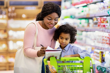 A mother and child review a grocery list while shopping.